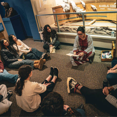 A group of students sitting on the floor in a circle while a tour guide reads from a book